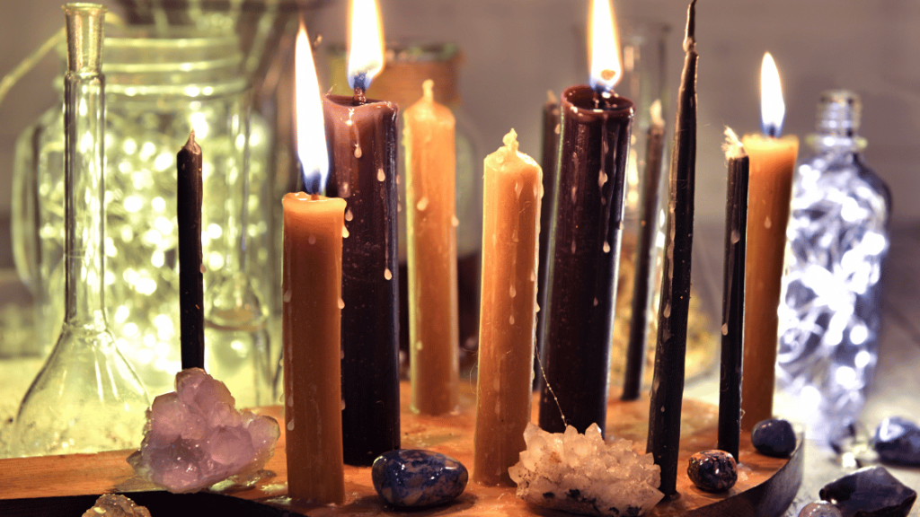 Płonące świece w różnych kolorach otoczone kryształami i akcesoriami wiccańskimi, tworzące magiczną atmosferę.