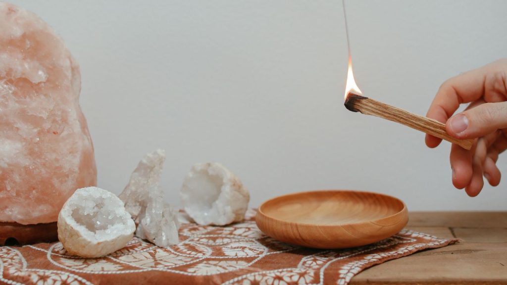 Dłoń trzymająca dymiące się drzewo palo santo okadzające dom w magiczne właściwości palo santo