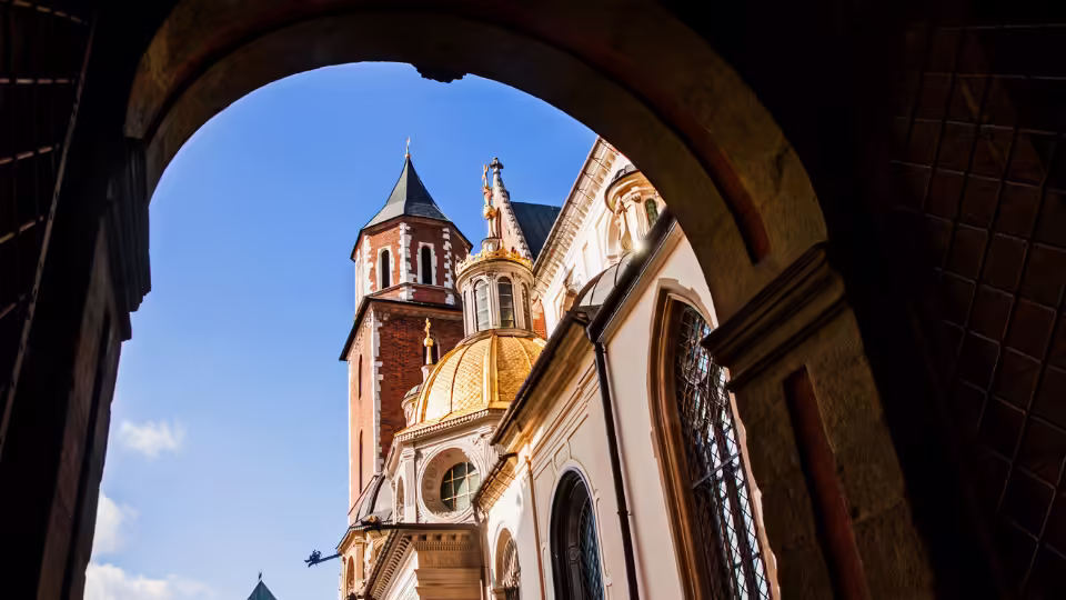Widok na Wawel w Krakowie przez łukowate przejście, z wieżami i kopułami katedry wawelskiej w tle. To miejsce jest znane jako najsilniejszy czakram w Polsce.