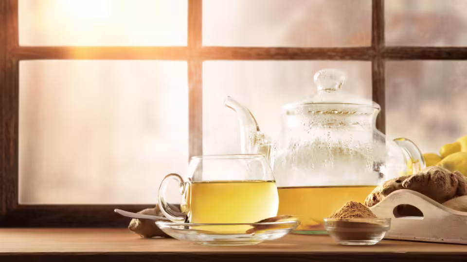 Świeżo zaparzona herbata z imbirem w szklanym dzbanku i filiżance, ustawiona na stole w ciepłym, domowym otoczeniu.