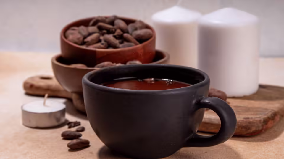 Kubek ceremonialnego kakao w towarzystwie ziaren kakaowca i świec – symbol duchowej atmosfery rytuału kakao.