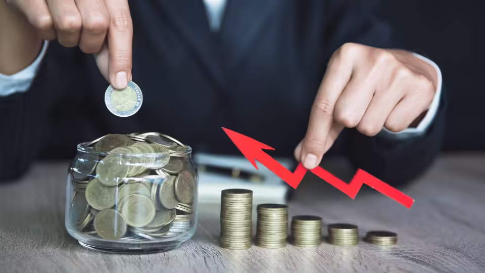 Osoba wkładająca monetę do słoika pełnego pieniędzy, obok rosnącego stosu monet i czerwonej strzałki symbolizującej wzrost. Obraz przedstawia proces oszczędzania i wzrostu finansowego, symbolizując afirmacje bogactwa oraz mądre zarządzanie finansami.