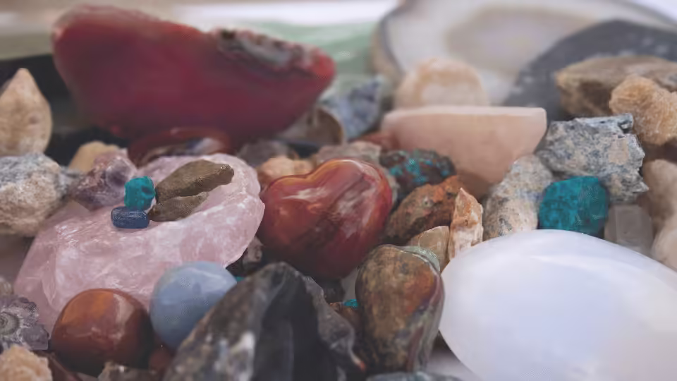 Zbiór różnych kamieni szlachetnych, w tym różowy kwarc, lapis lazuli i inne minerały, ułożone na białej powierzchni.