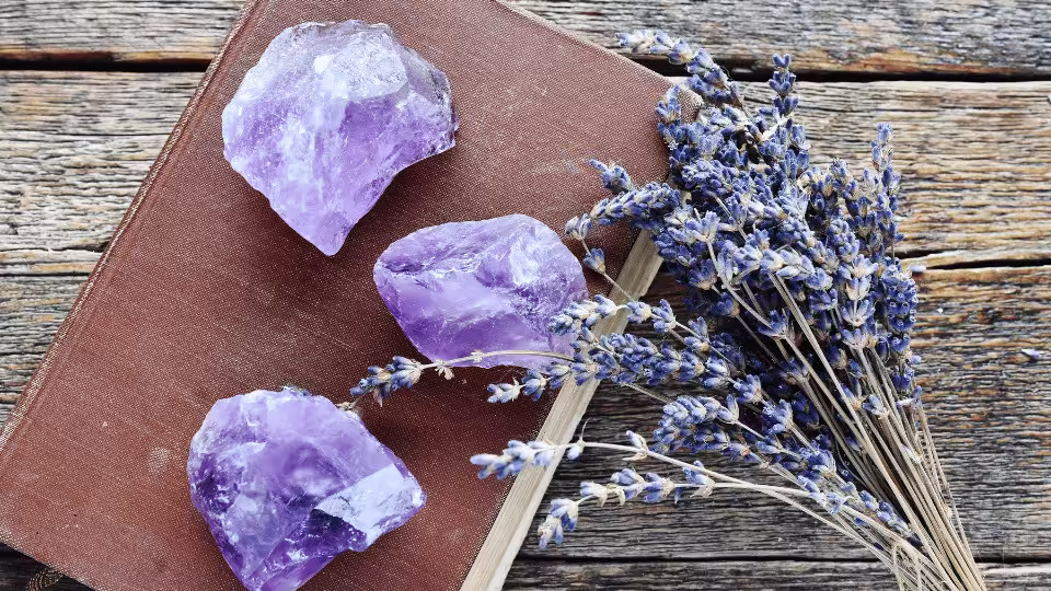 Ametyst w surowej formie ułożony na książce obok suszonej lawendy, symbolizujący spokój, harmonię i duchową ochronę.