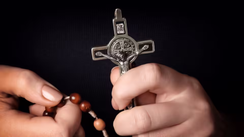 Osoba trzymająca różaniec i krzyż Świętego Benedykta, symbol ochrony i wiary chrześcijańskiej.