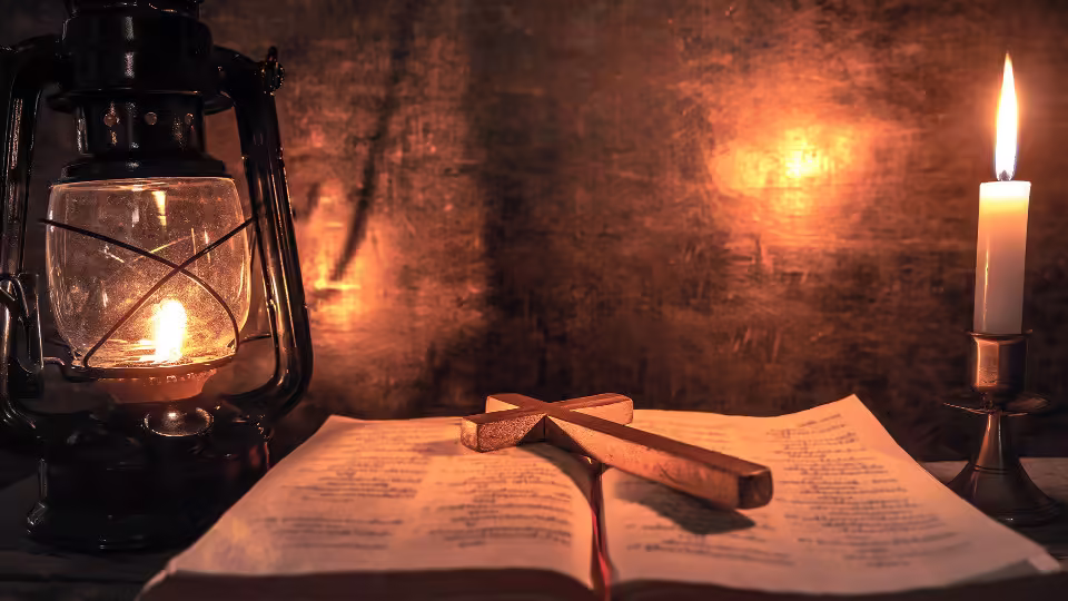 Krzyż leżący na otwartej księdze przy lampie naftowej i świecy, symbolizujący wiarę i duchową refleksję.