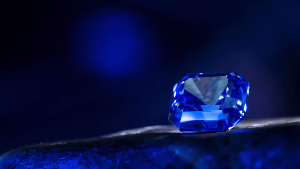 Wyjątkowo szlifowany szafir w głębokim, intensywnie niebieskim kolorze, spoczywający na ciemnym tle, ukazujący swoje lśniące fasety.