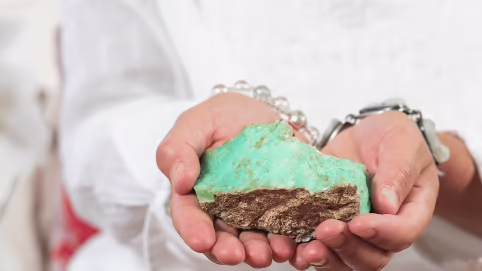 Duży kawałek chryzoprazu trzymany w dłoniach osoby, ukazujący jego surową formę i naturalny zielonkawy kolor.