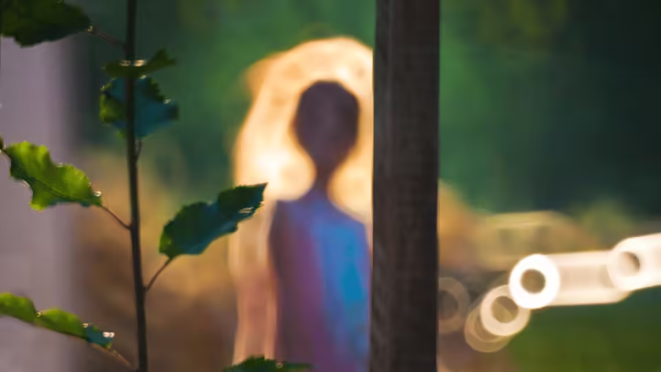 Postać otoczona jasnym blaskiem aury, rozmyta sylwetka w otoczeniu natury, nawiązująca do energii i kolorów aury człowieka.