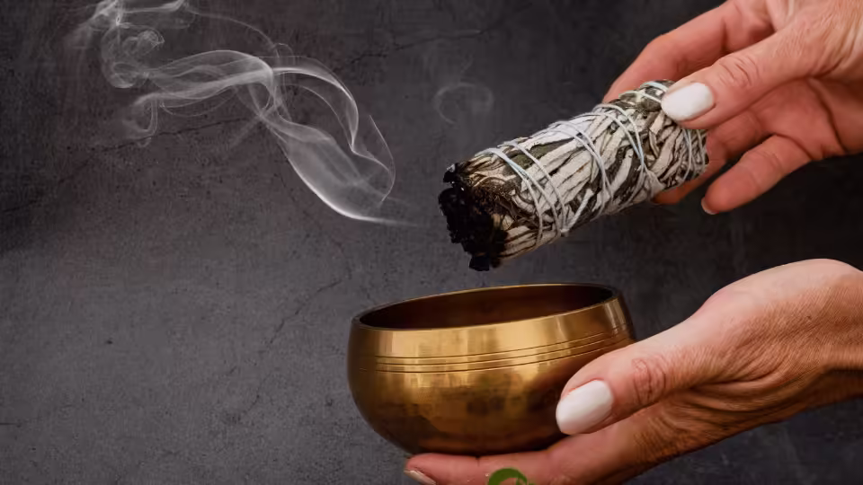 Dymiąca szałwia i mosiężna miseczka w dłoniach podczas rytuału oczyszczania energetycznego