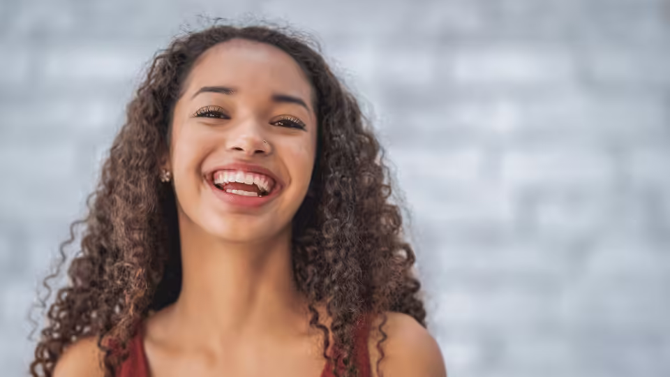 Młoda kobieta z kręconymi włosami, szeroko uśmiechnięta, emanująca radością i pozytywną energią.