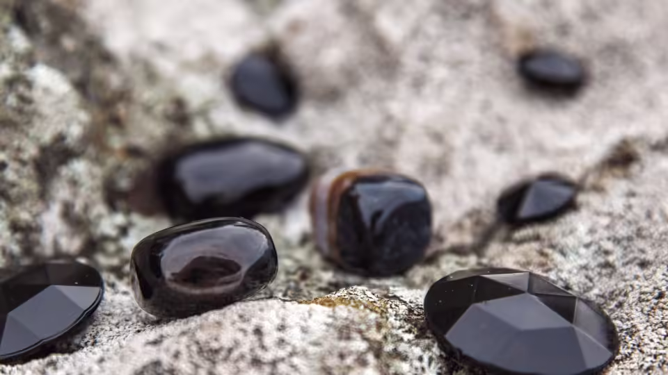 Czarne kamienie ozdobne leżące na skalistym podłożu, symbolizujące ochronę i stabilność energetyczną.