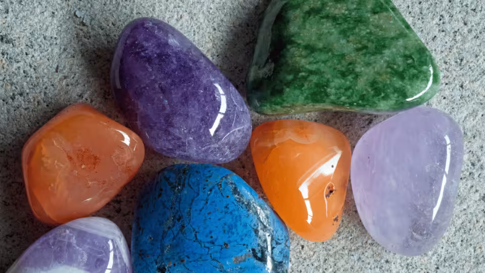 Kolorowe, polerowane kamienie szlachetne, w tym ametyst, karneol i lapis lazuli, leżące na kamiennej powierzchni.