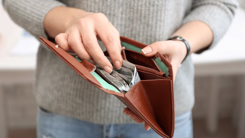 Osoba trzymająca brązowy portfel z pieniędzmi i liściem laurowym, używanym w rytuale przyciągania obfitości.