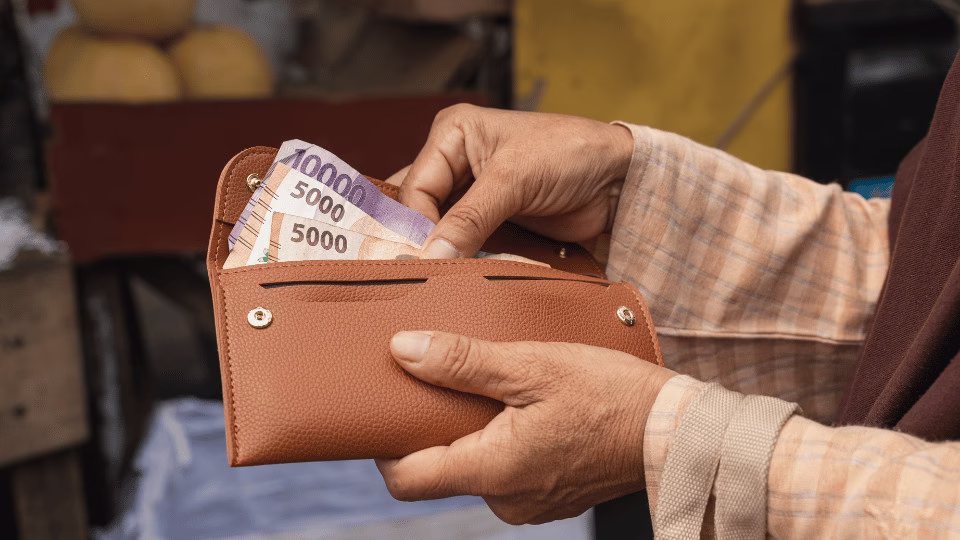 Osoba trzymająca brązowy portfel z banknotami i liściem laurowym w środku, symbolizującymi rytuał przyciągania pieniędzy i dostatku.