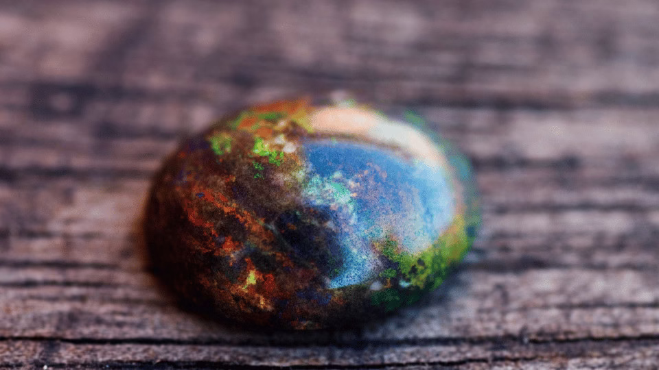 Zbliżenie na czarny opal o hipnotyzujących, wielobarwnych refleksach na tle naturalnego drewna, podkreślające jego unikalne piękno.