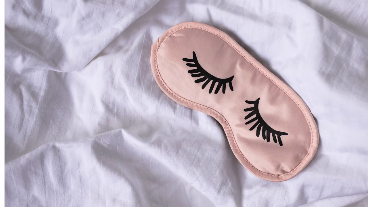 Różowa opaska na oczy, leżąca na białej pościeli -symbolizuje sen 