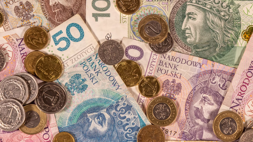 Rozrzucone polskie banknoty i monety – złotówki o różnych nominałach symbolizujące dostatek i pieniądze.
