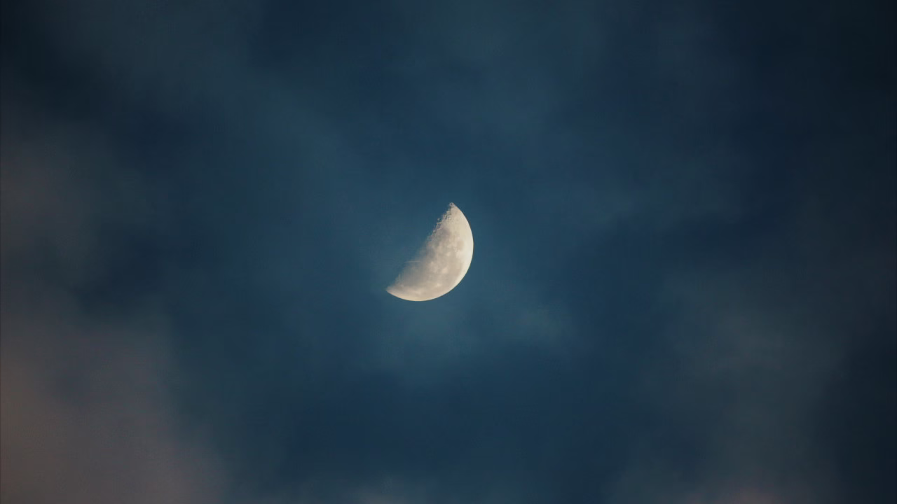 Nocne niebo z wąskim sierpem Księżyca wśród gwiazd i lekkich chmur.”