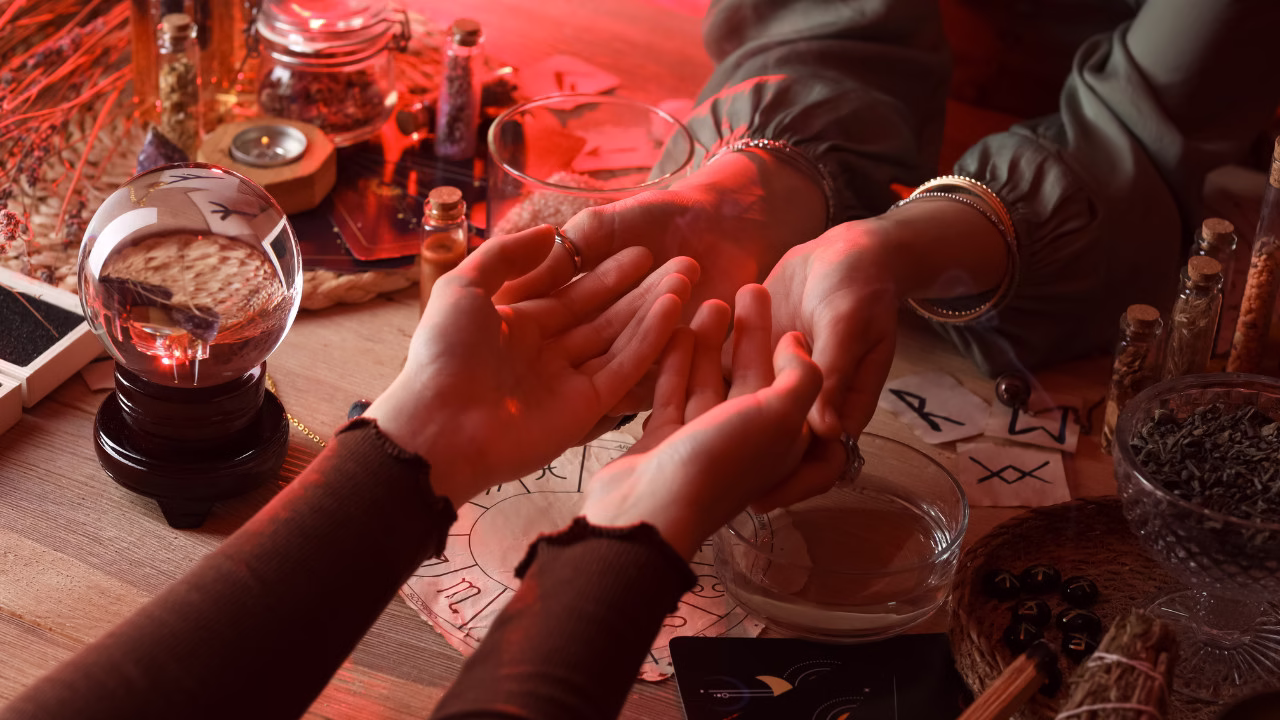 Dwie osoby przy stole z akcesoriami ezoterycznymi podczas wróżenia z dłoni